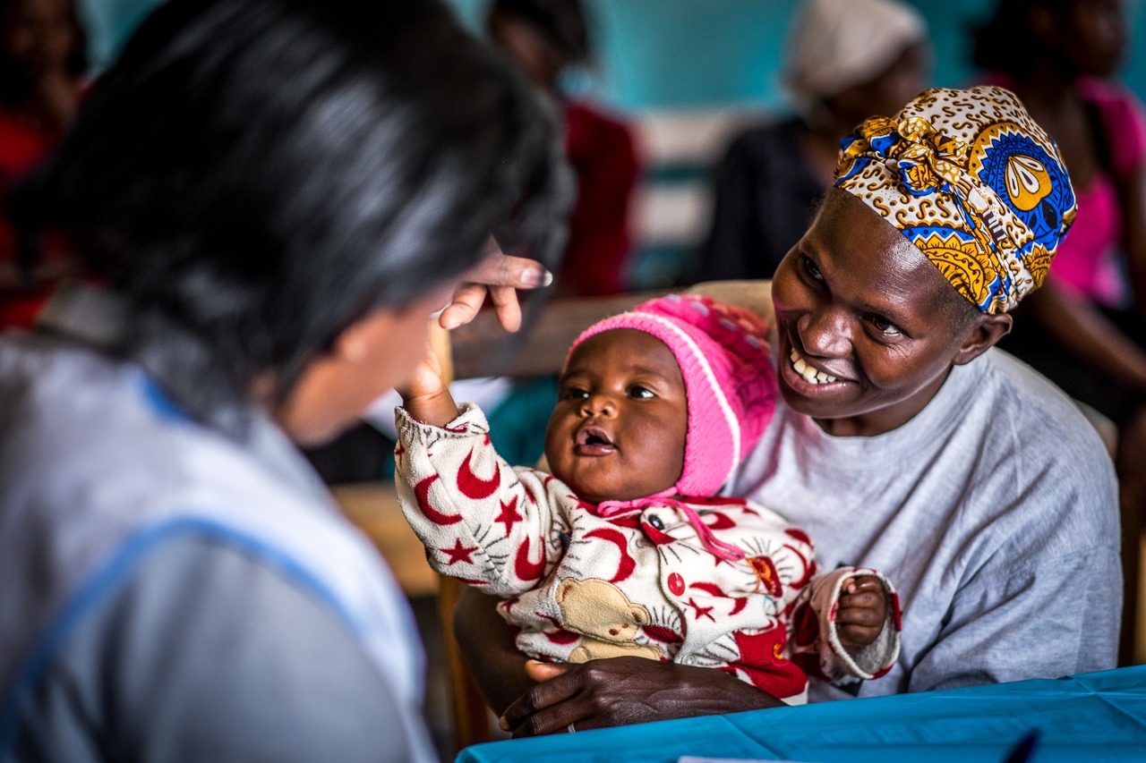 Healthcare provider examining an infant while supporting a mother in a local clinic.